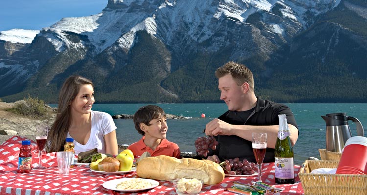 A family seated at a picnic table, having a picnic at Lake Minnewanka