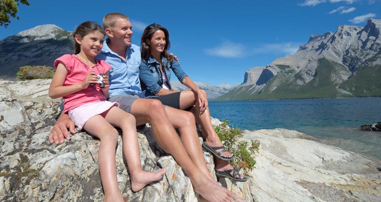 A family sitting on beach looking at Lake Minnewanka