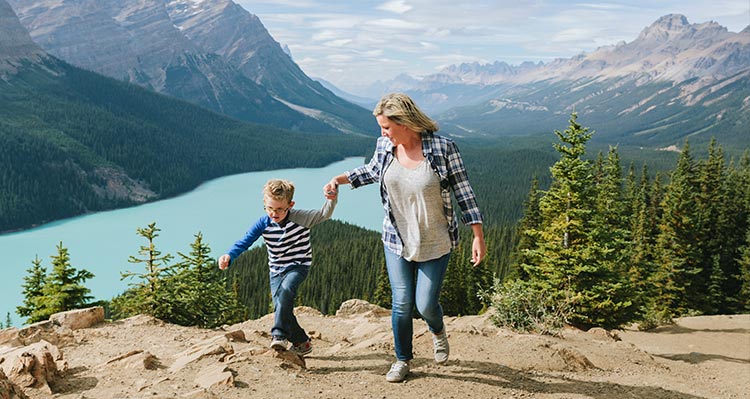 A mom and child walk on a path high above a blue lake.