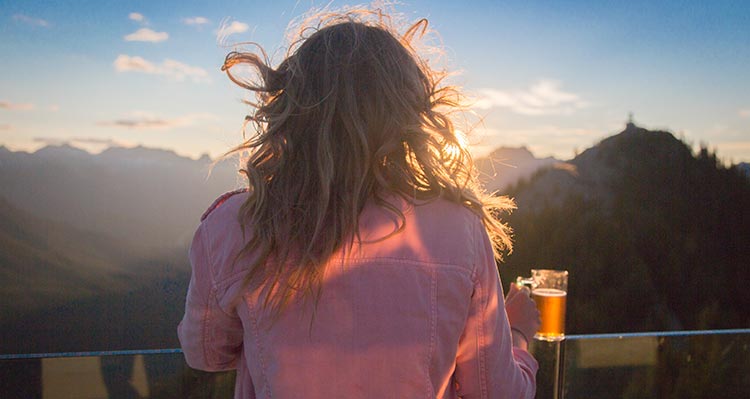 A woman stands at a railing looking towards the sunset