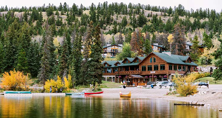 A wooden lodge close to a lake with some canoes at the water's edge.