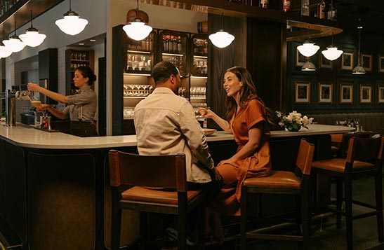 A couple sits at the Brazen bar with a bartender to the side.