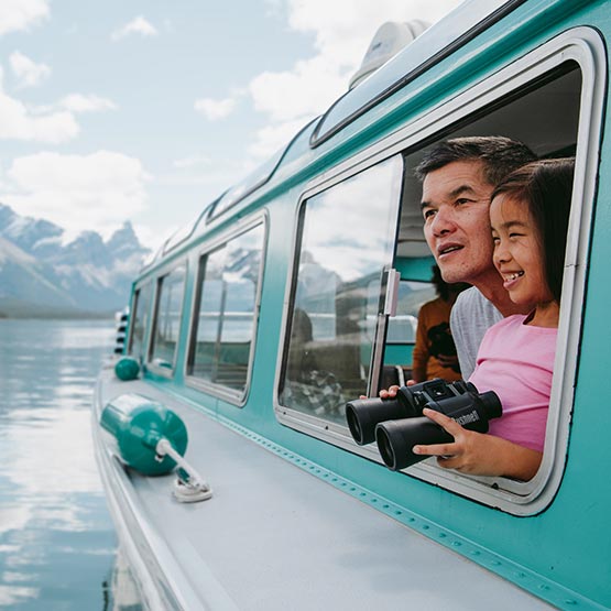 A parent and child look out the window of a boat on a calm lake.