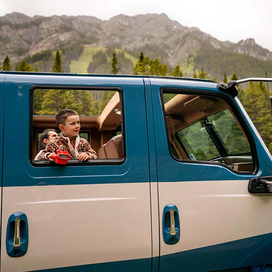 A child looks out the window of a historic-style touring car.