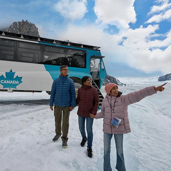 A family walking on a glacier next to a blue Ice Explorer vehicle.