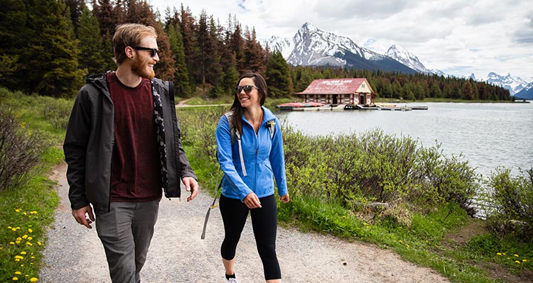 Two people walk on a trail next to a calm lake.