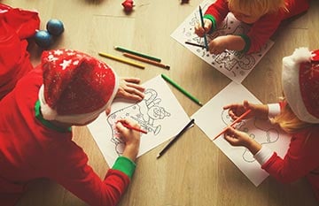 Three children colour on Christmas-themed colouring sheets