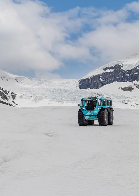 An all-terrain Sherp vehicle drives on a glacier between mountains.
