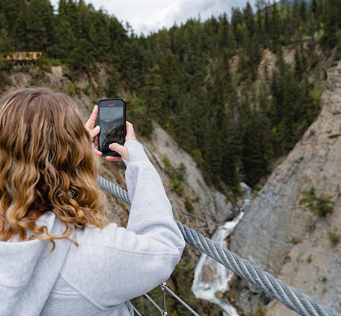 A person takes pictures from a suspension bridge above a rushing river.