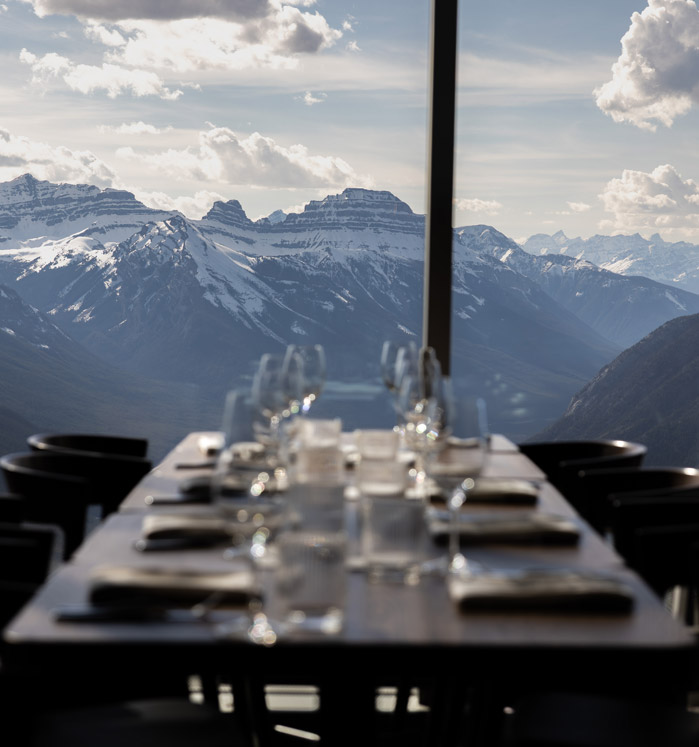 A large window-side table set with dishes and glassware, with a mountain view out the window.