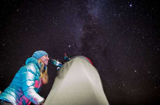 A woman looks through a telescope at the night sky.