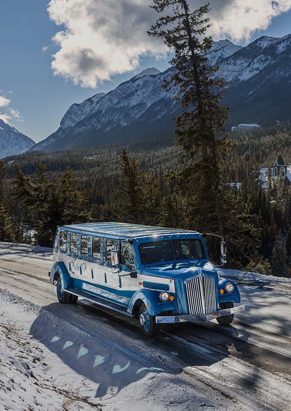 A vintage style touring automobile on a snowy road above forested mountiansides.