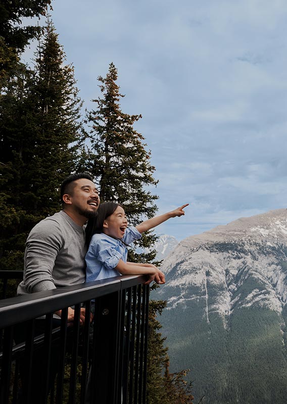 A parent and child watch a Banff Gondola cabin ascend to the upper terminal.
