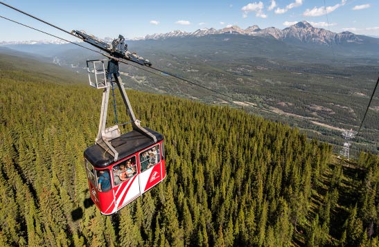 A red Jasper SkyTram car ascends up a forested mountainside.