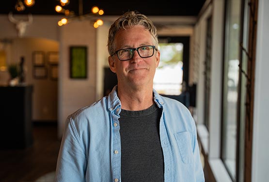 A portrait of Mike Day, a man wearing glasses and a blue shirt.