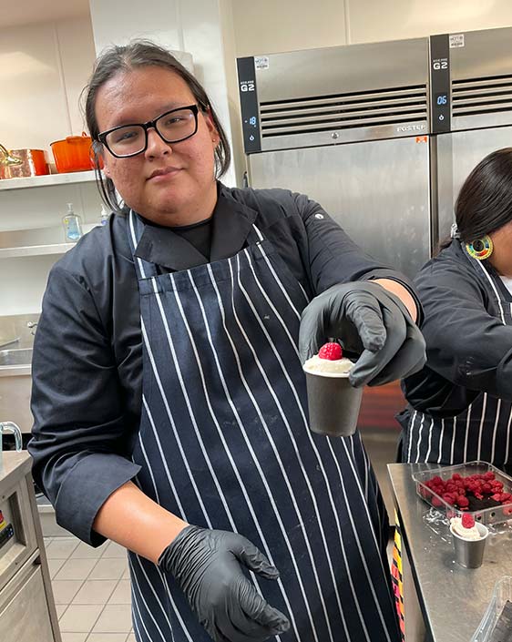 A young chef holds a pastry in an commercial kitchen