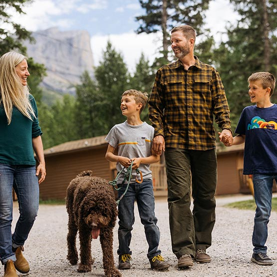 A family walking with a dog near wooden cabins.