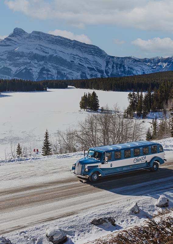 A vintage style touring automobile driving past a frozen lake.