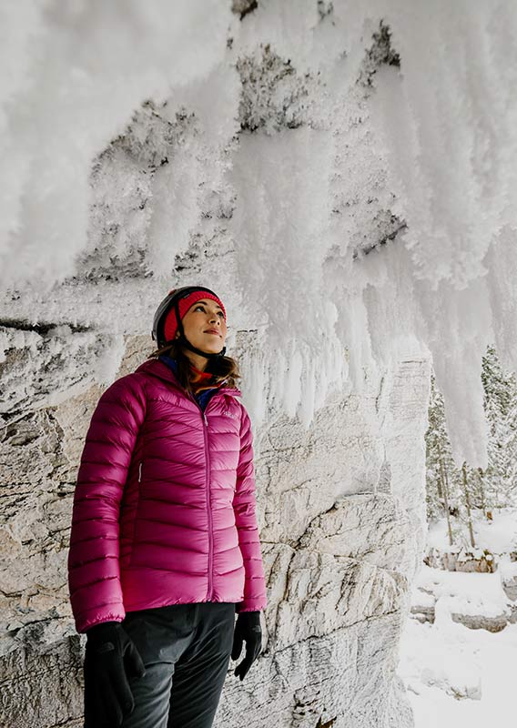 A woman stands under a frozen cliffside.