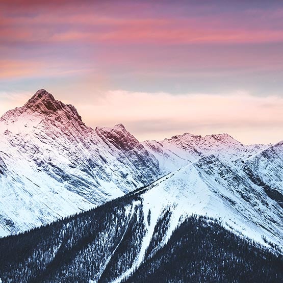 A mountain landscape of snow-covered peaks and pink glowing sky.