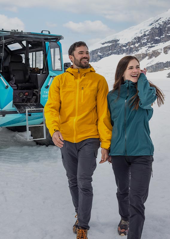 Two people walk away from an Ice Odyssey vehicle on a glacier.