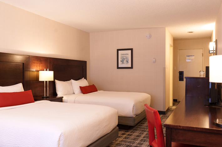 A hotel room with two queen beds with white bedding and red pillow cases.