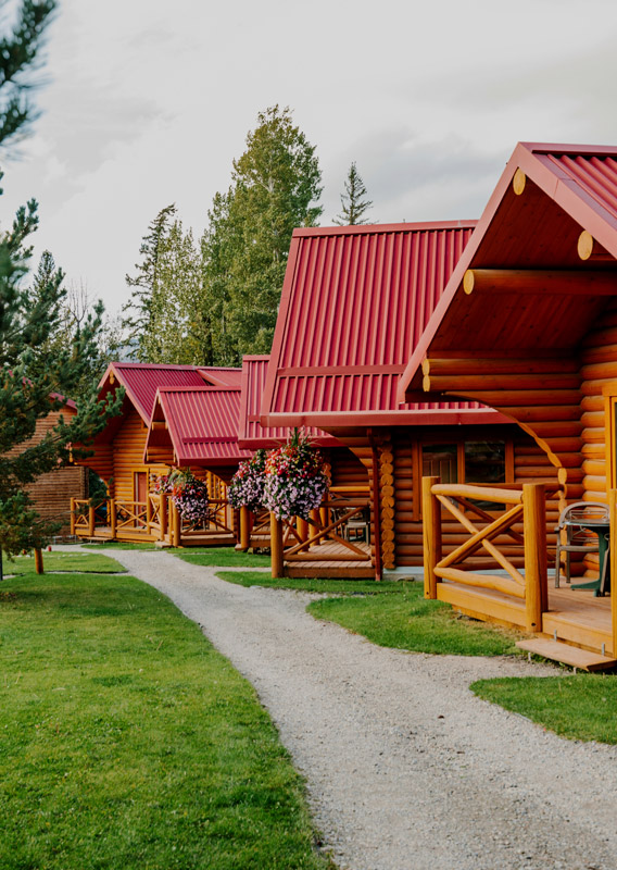 Wooden cabins with red roofs and flowers at the enterance set along a path beside a park.