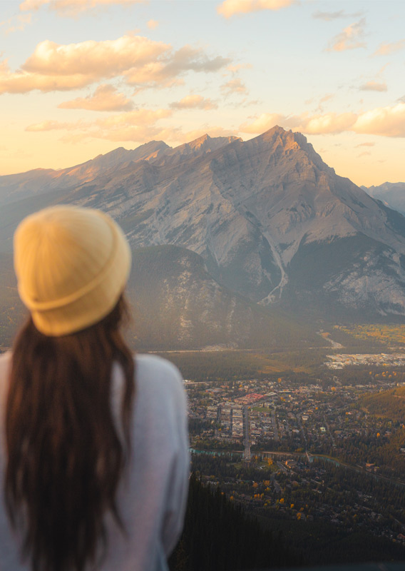 A person standing at a viewpoint, looking at a town and mountain at sunset in the fall.